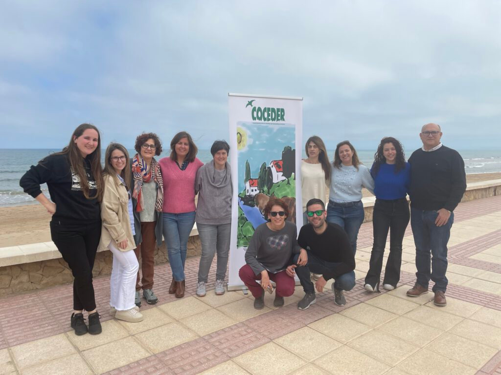 Grupo de personas que forman el equipo técnico alrededor de la imagen de Coceder con fondo de la playa