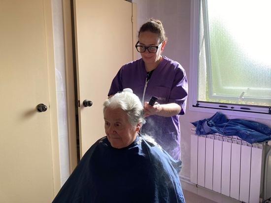 Una mujer de pie corta el pelo a una señora sentada