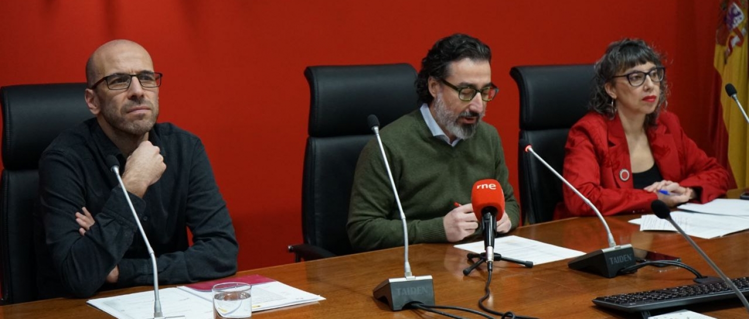 Dos hombres y una mujer sentados en una mesa hablando con micrófonos