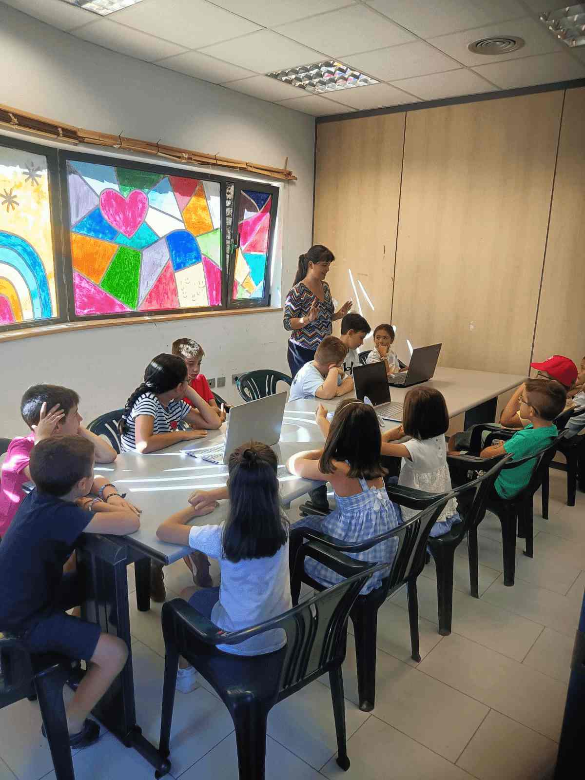 un grupo de niños y niñas sentados trabajan con ordenadores en una clase