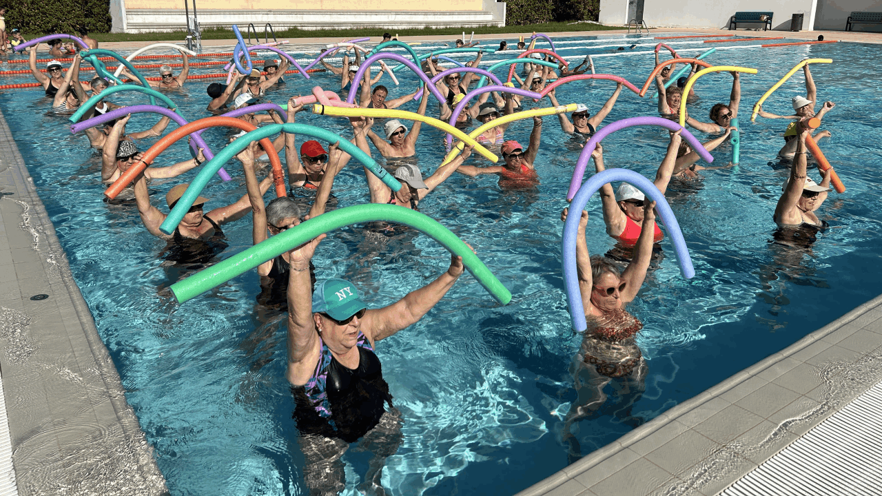 Un grupo de personas dentro de una piscina haciendo ejercicio con churros de colores