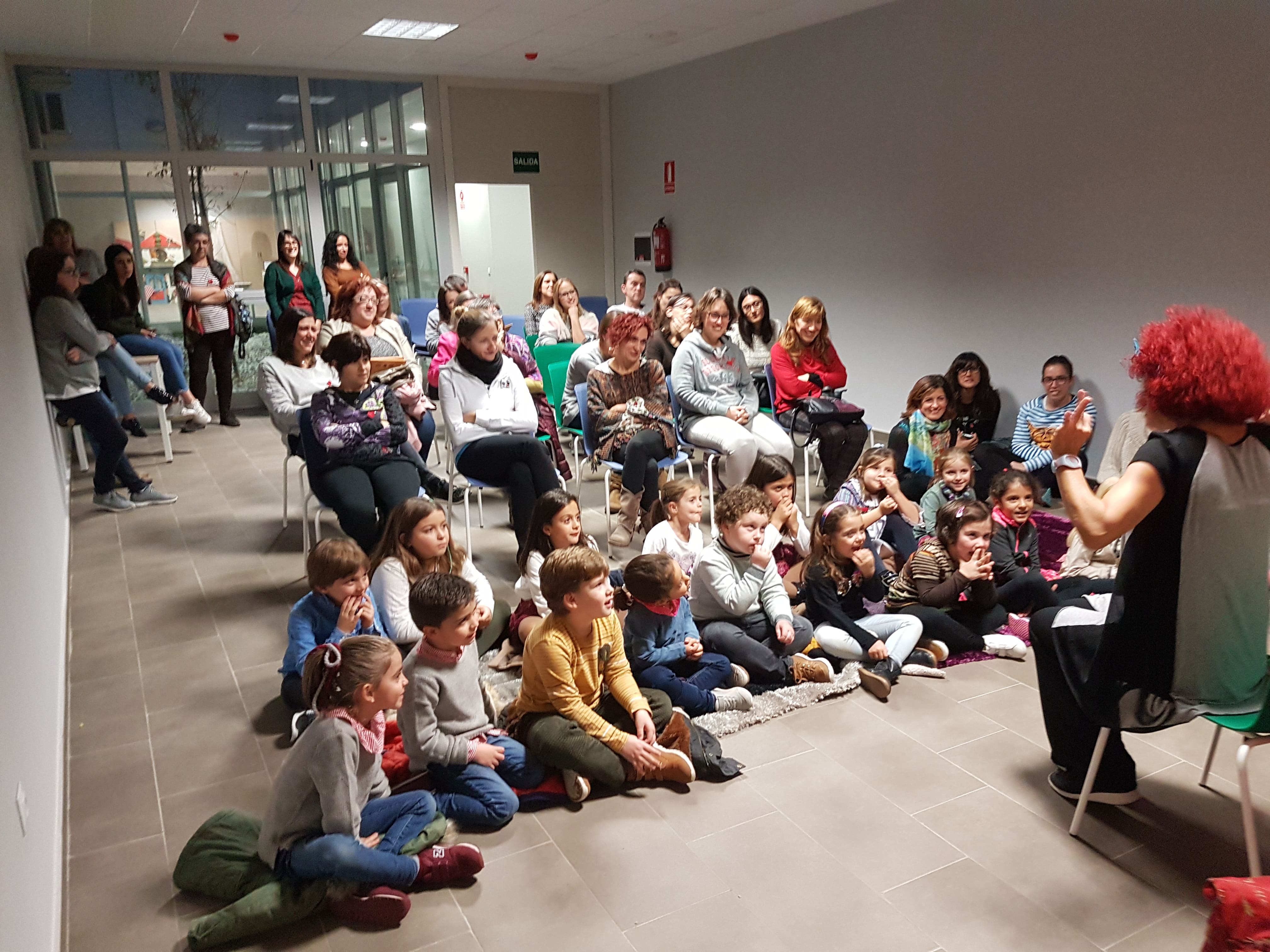 grupo de menores sentados escuchando a una persona contar un cuento