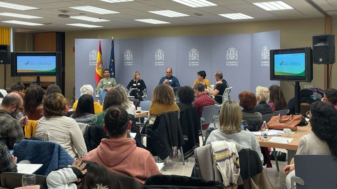 Un grupo de personas escuchan a cinco personas hablando en un escenario