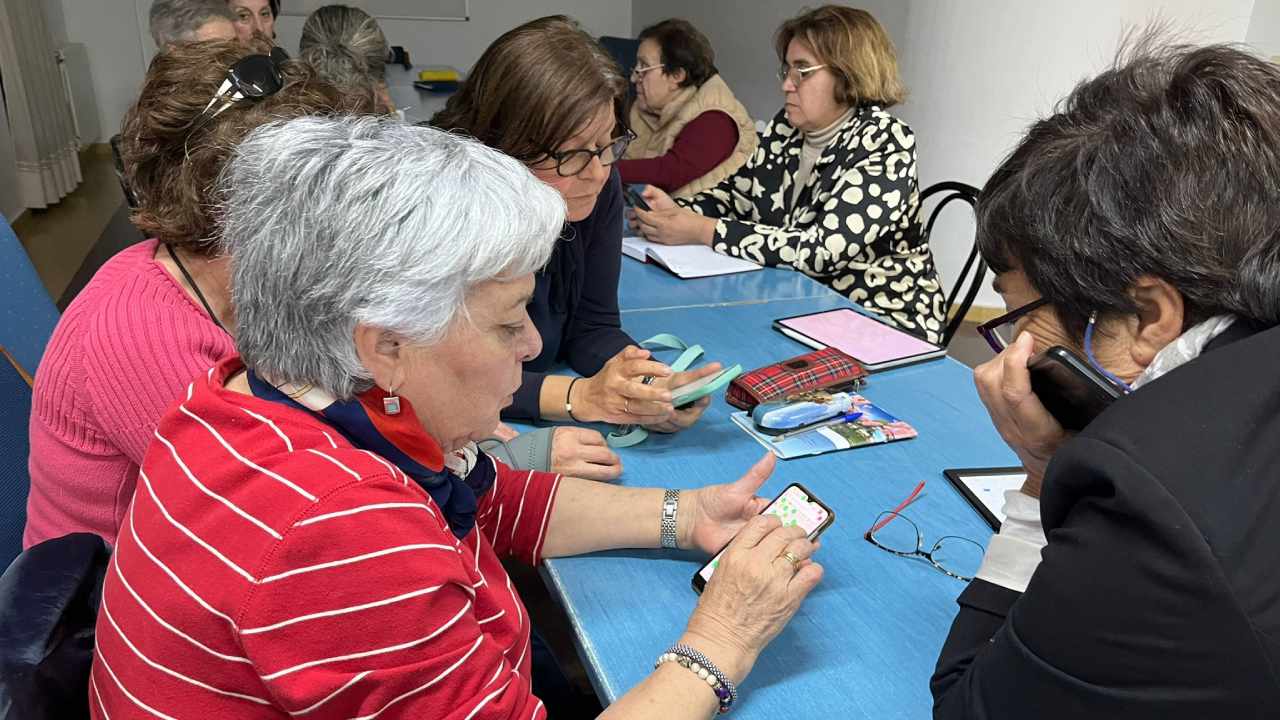 Un grupo de señoras alrededor de una mesa manejando un teléfono móvil