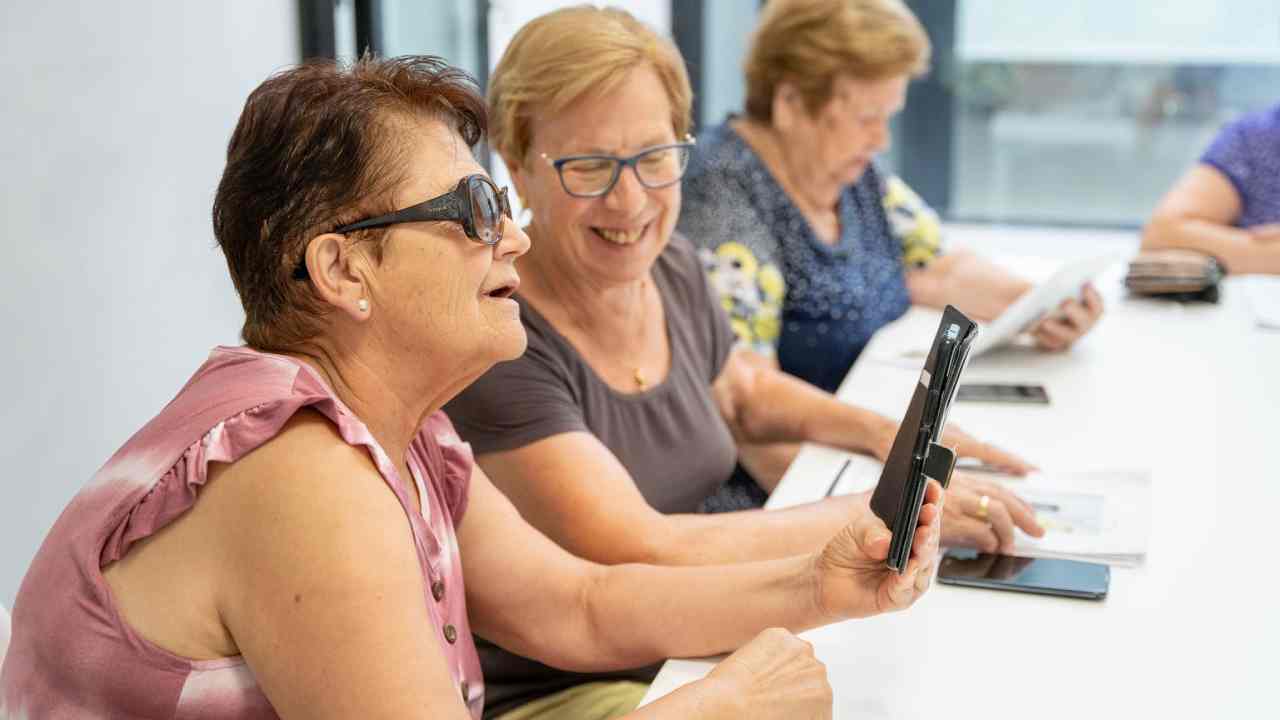 Dos mujeres mayores contemplan sonrientes un teléfono móvil