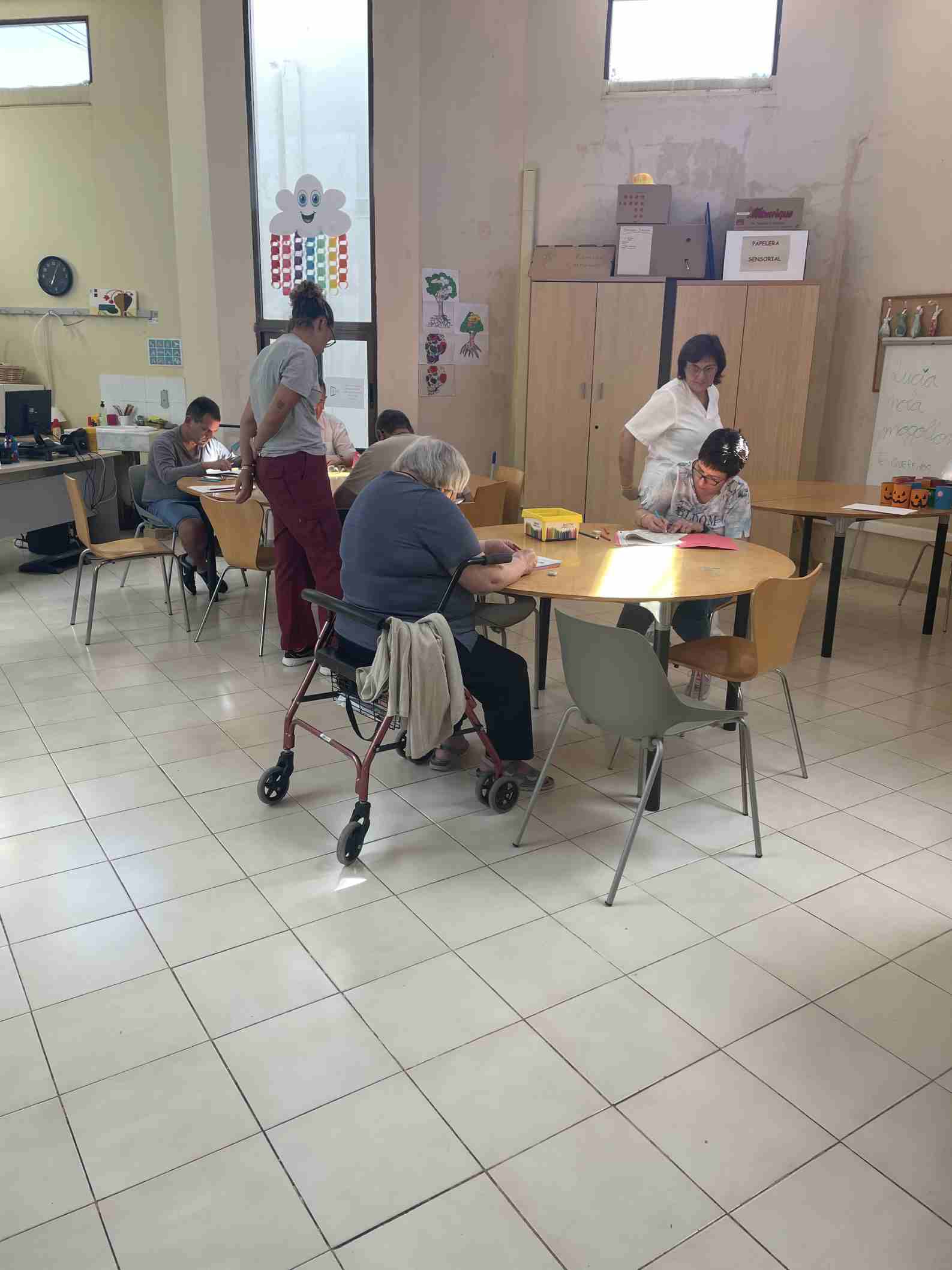 Personas en una mesa dibujando con dos mujeres cuidadoras