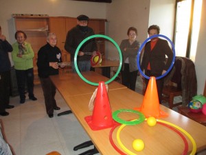 Grupo de personas mayores en una sala con conos, aros y pelotas