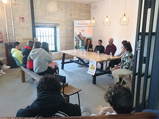 Foto de la jornada con un grupo de personas alrededor de una mesa como presentadores de la jornada y un grupo de jóvenes escuchandola