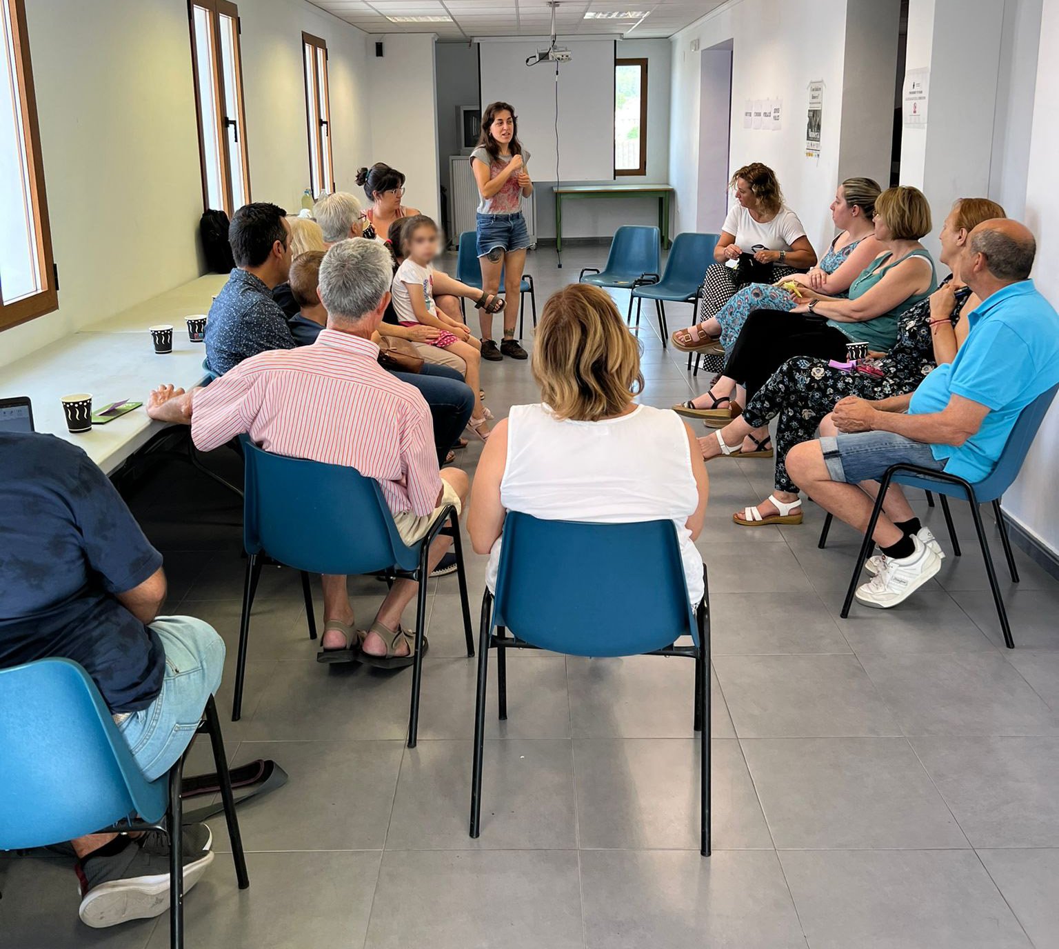 Grupo de personas sentadas en círculo en un aula escuchando a una mujer
