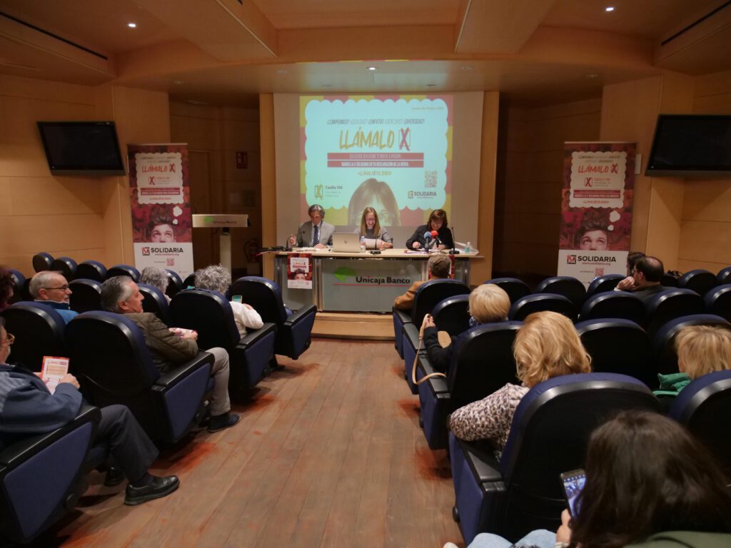 Foto de un salón con personas escuchando a los oradores que presentan la campaña de la X solidaria