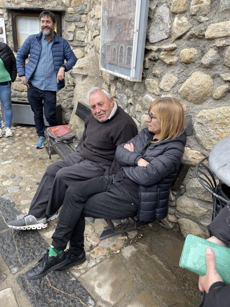 Personas conversando unas a pie y otras sentadas en un banco de una zona rural